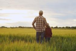 Man and child standing in a green field looking away