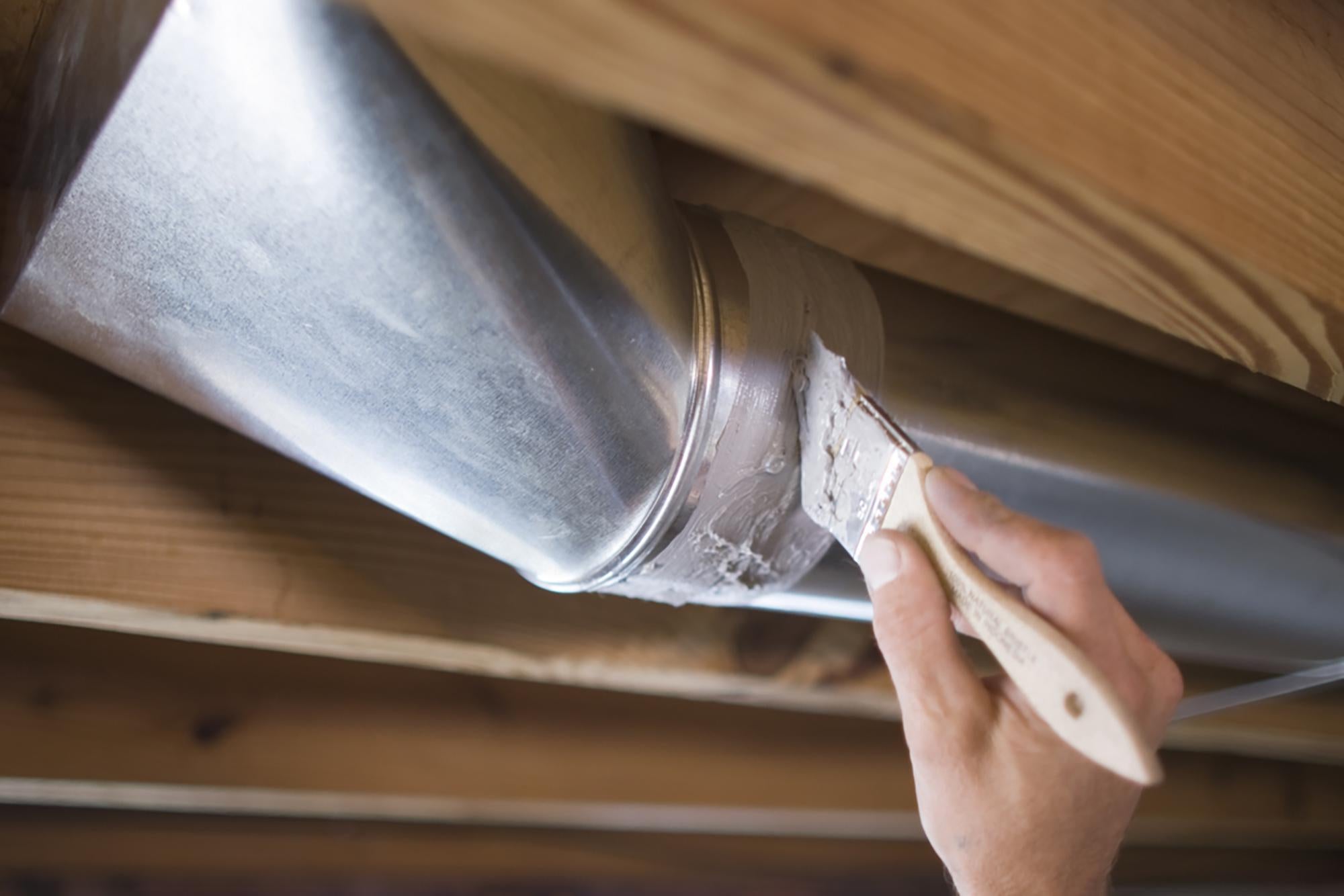 Man's hand with paintbrush sealing air ducts with caulk