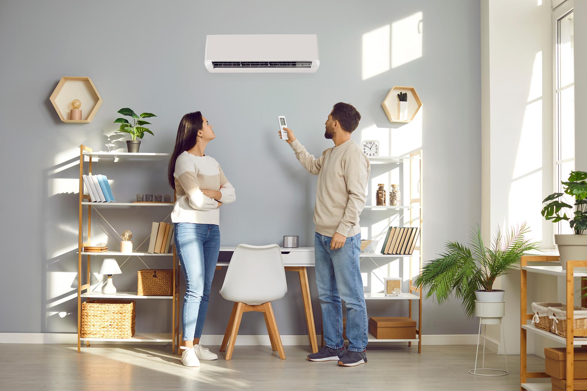 Male and female inside a home office looking at the indoor unit of a ductless heat pump holding a remote to change the temperature