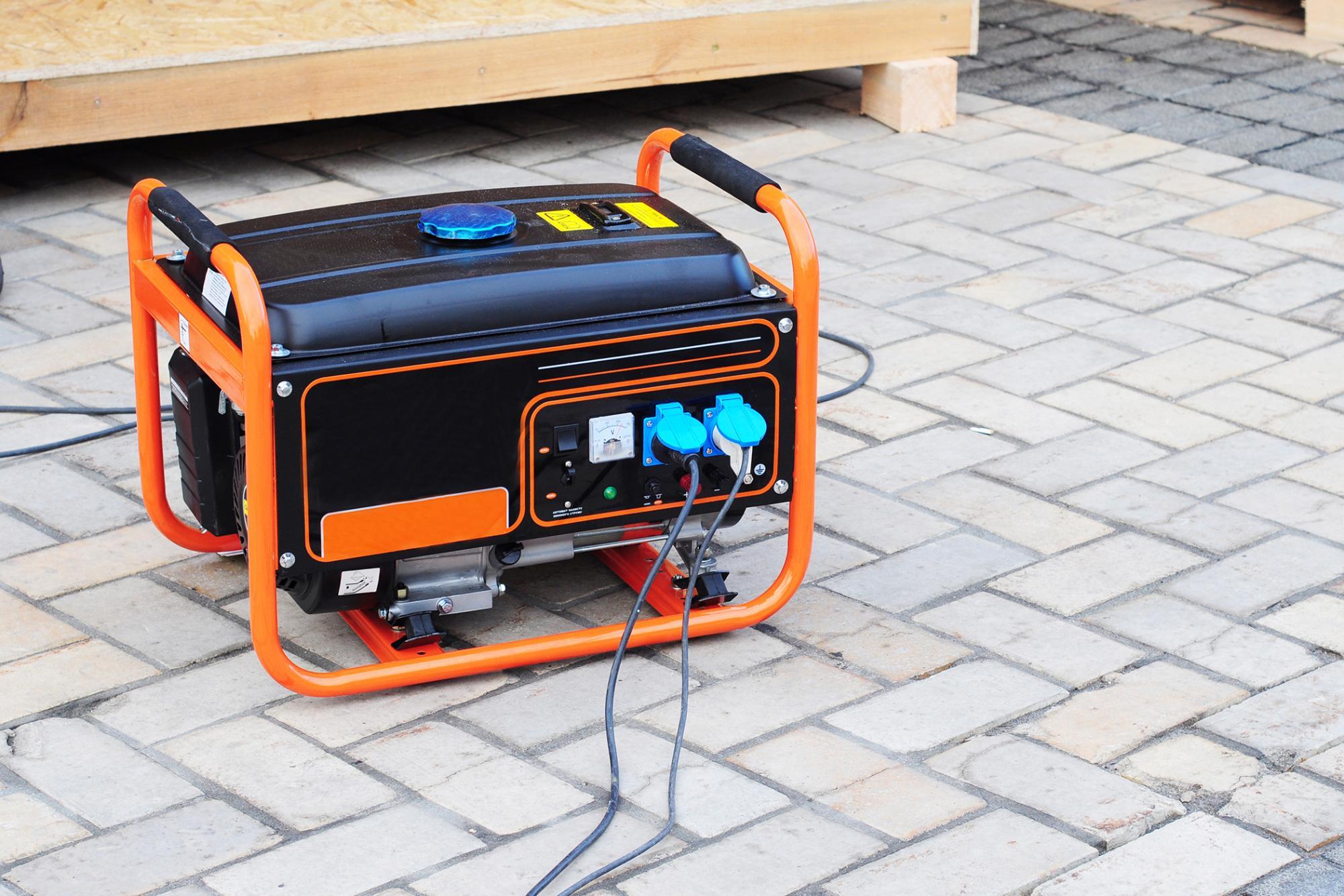 Portable generator sitting outside on cobblestone with cords plugged into it