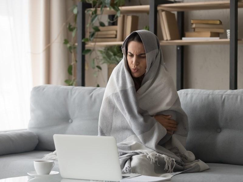 woman cold in blanket on couch using laptop